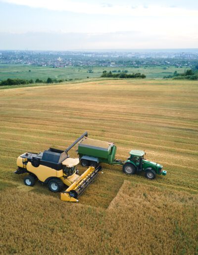 Aerial view of combine harvester unloading grain in cargo trailer working during harvesting season on large ripe wheat field. Agriculture and transportation of raw farm products concept.